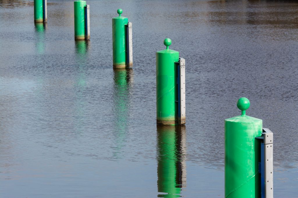 A serene view of green mooring poles reflected in calm water at a port.